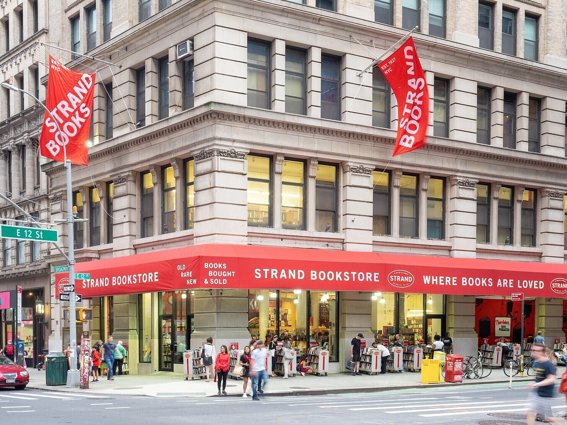 Strand Bookstore's exterior with red awnings and people browsing the outdoor bookshelves